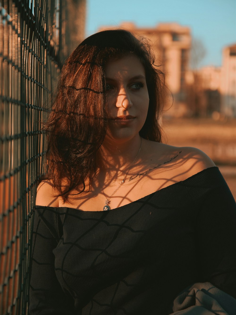 woman in black off shoulder shirt standing beside black metal fence during daytime
