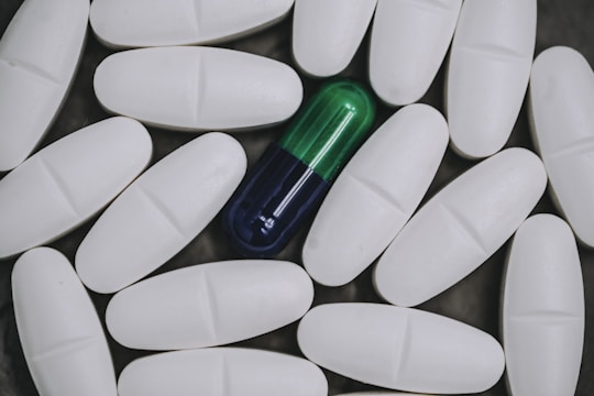 A collection of white oval tablets surrounding a single blue and green capsule placed at the center, creating a contrast between the homogeneous group of tablets and the distinct capsule.