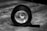 A black and white photograph shows a large roll of tape lying on its side on a wooden surface, with a smaller rolled-up object perfectly aligned inside it. The background is blurred, drawing attention to the rolls of tape.