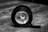 A black and white photograph shows a large roll of tape lying on its side on a wooden surface, with a smaller rolled-up object perfectly aligned inside it. The background is blurred, drawing attention to the rolls of tape.