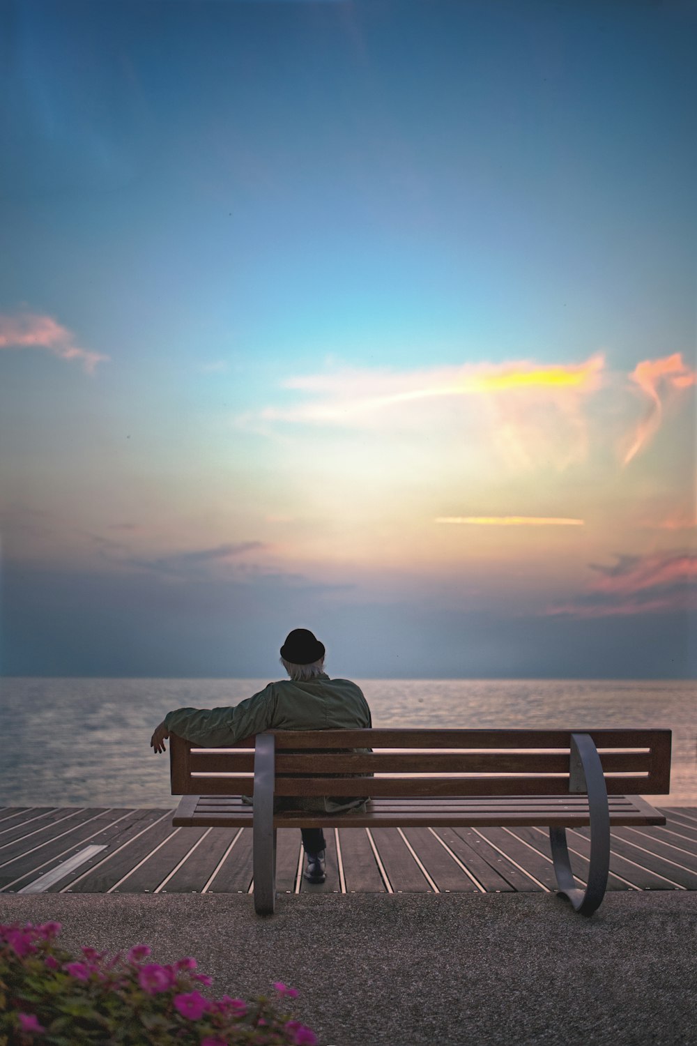 Hombre sentado en un banco de madera marrón frente al mar durante el día