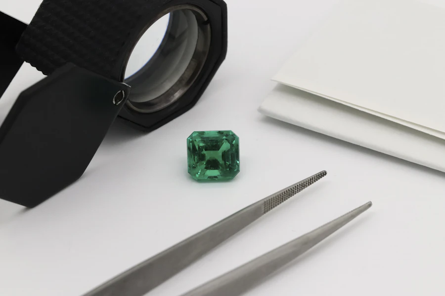 Emerald cut green gemstone beside jeweler's tweezers and a loupe