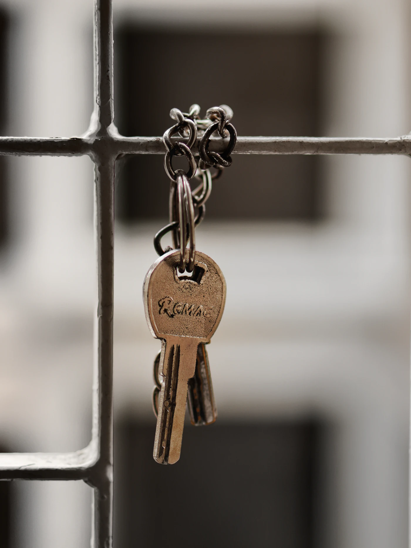 A set of worn brass keys on a ring hanging from a metal window grille in front of an apartment doorway