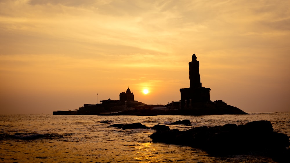 silhouette of building on rock formation near body of water during sunset