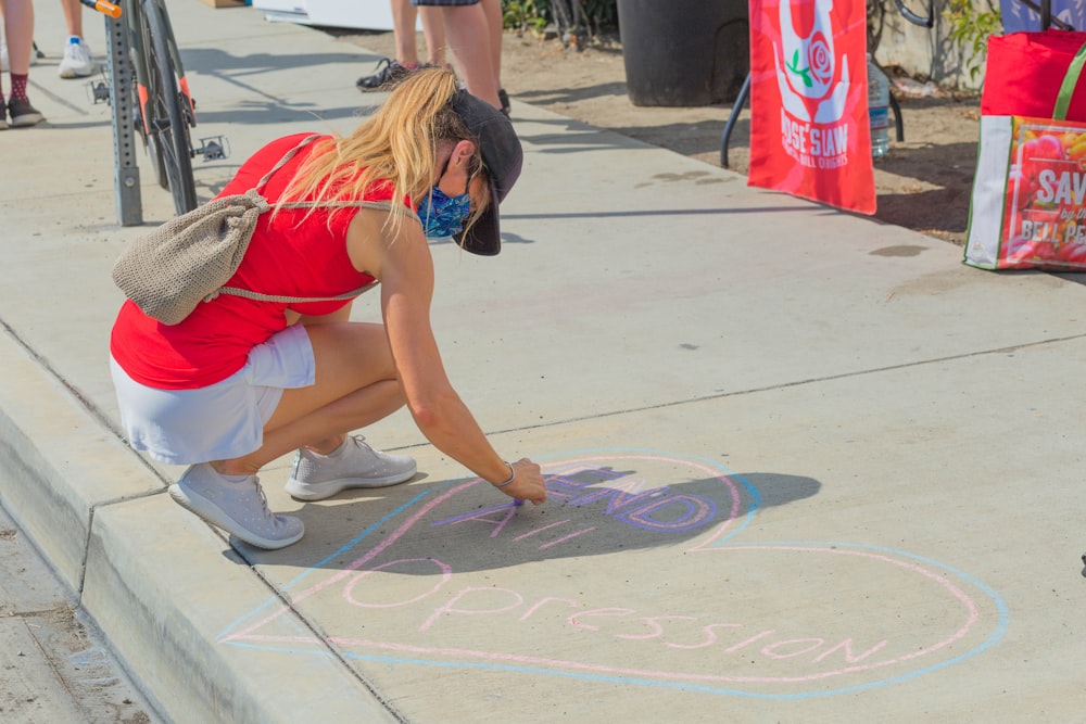 woman in red and white tank top and white shorts sitting on concrete floor during daytime