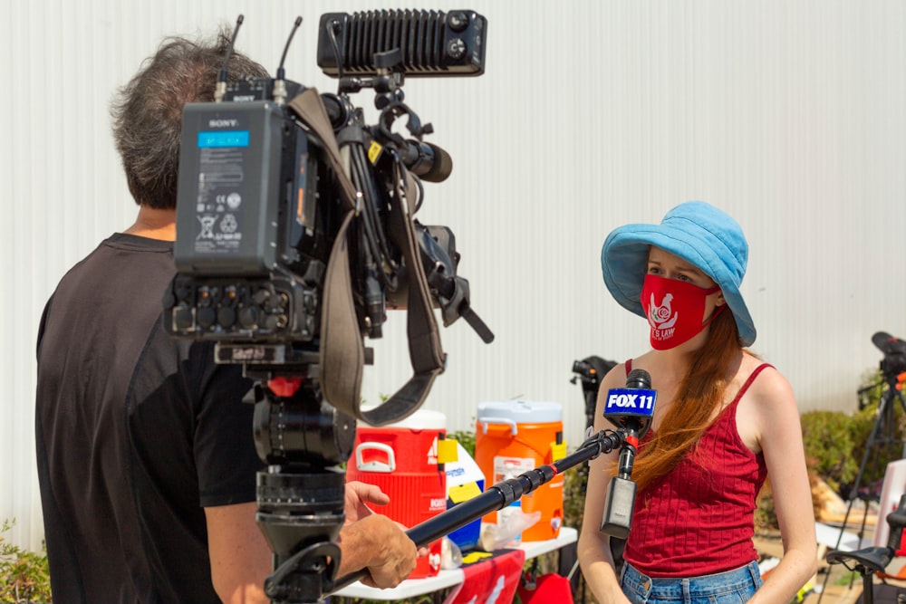 woman in orange shirt and blue denim jeans standing in front of black and gray camera