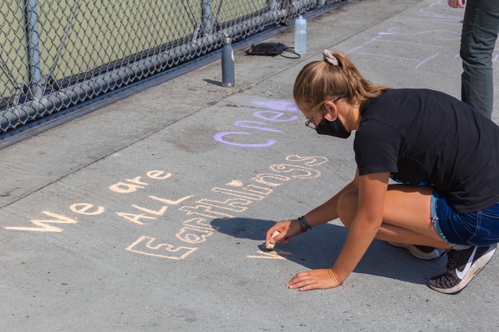 woman in black t-shirt and brown shorts sitting on concrete pavement