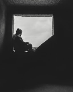 A quiet moment of a person sitting by a window, lost in thought on a soft, overcast day.