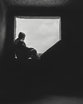 A quiet moment of a person sitting by a window, lost in thought on a soft, overcast day.