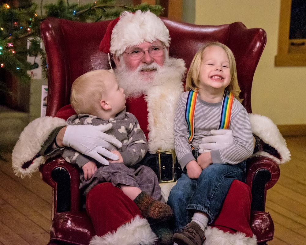 man in santa claus costume sitting on red leather armchair carrying baby in white fur coat