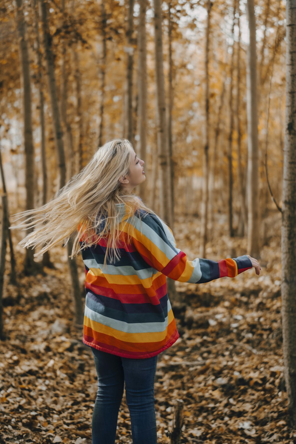 woman in orange yellow and blue striped long sleeve shirt standing on brown dried leaves during