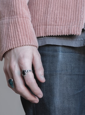 Close-up of a hand wearing layered silver rings with a soft pastel background.