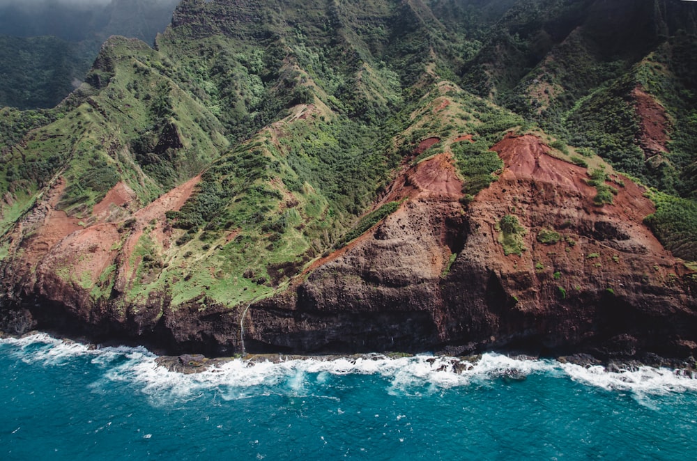 Montaña verde y marrón junto al mar azul durante el día