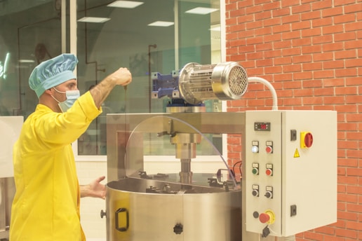 homem paramentado com roupa amarela, touca e máscara em fábrica trabalhando em condição especial