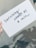 A hand is holding a white card with black handwritten text that reads 'Surviving counts as a win'. The background appears slightly blurred with plant shadows visible.
