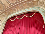 An antique puppet stage with ornate golden details and faded painted backdrop.