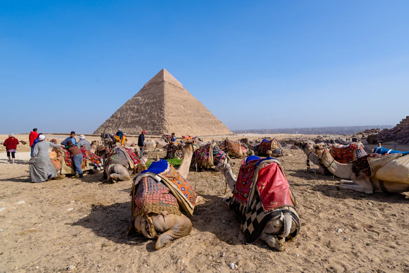 People sitting on brown sand near pyramid under blue sky