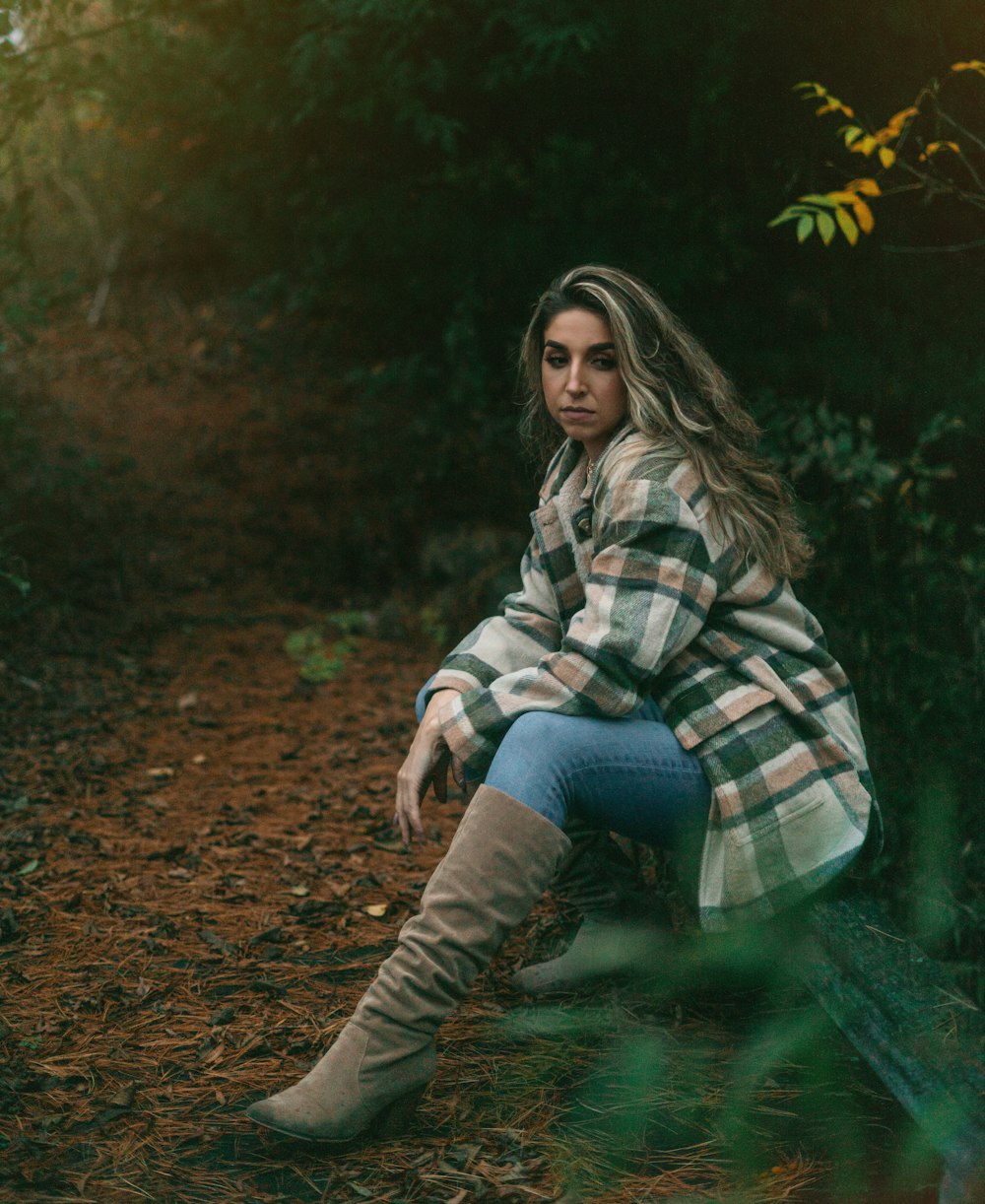 woman in white and black plaid long sleeve shirt and blue denim jeans sitting on brown