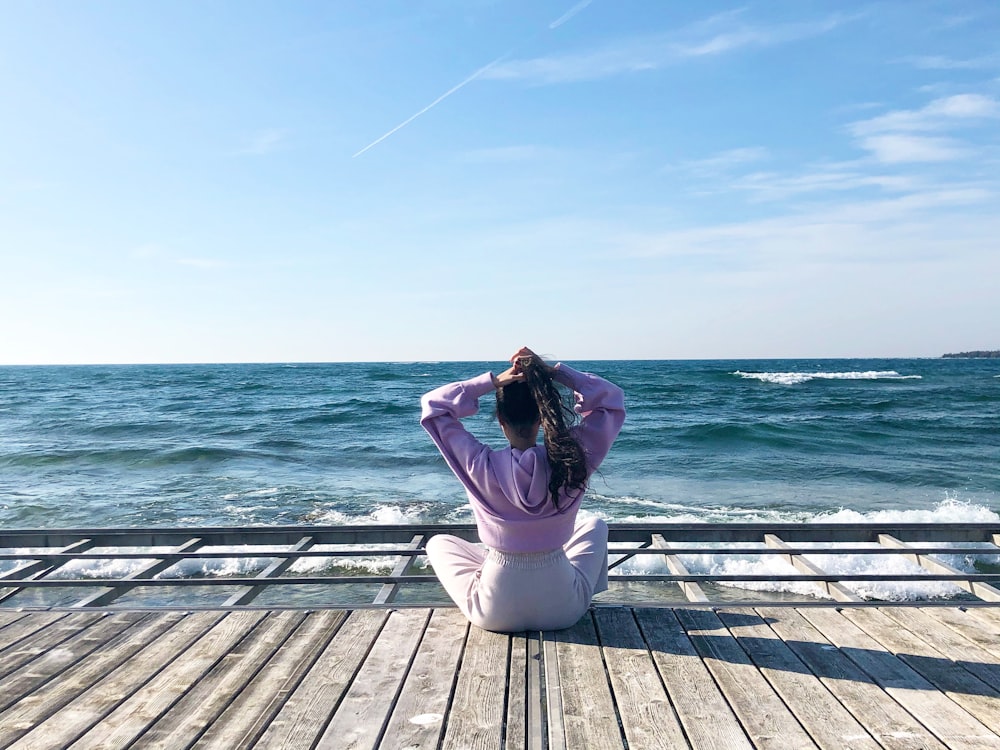 woman in white pants sitting on wooden dock during daytime