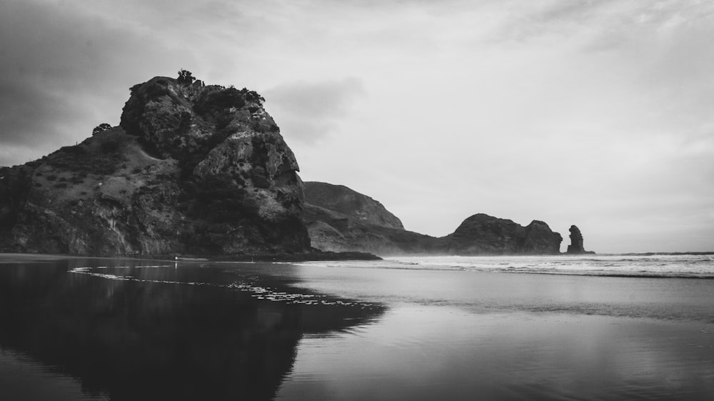 grayscale photo of rocky mountain near body of water