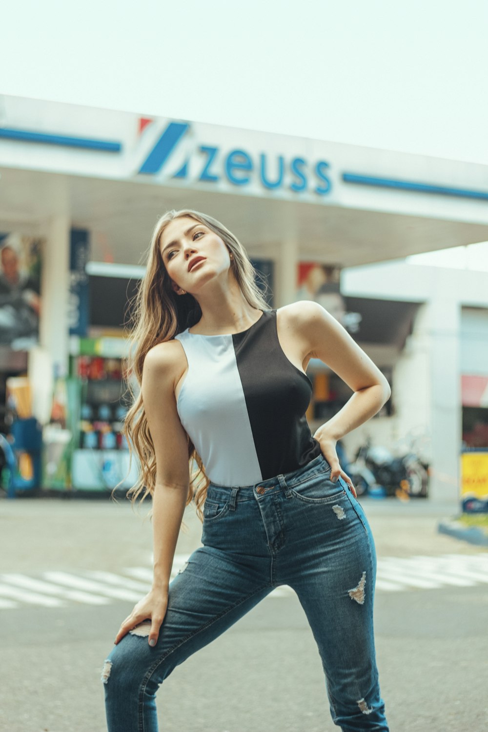woman in white tank top and blue denim jeans standing on street during daytime