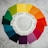 A circular arrangement of Pantone color swatches on a textured gray surface. The swatches form a color wheel with shades transitioning from greens to blues, purples, reds, oranges, and yellows. Each swatch is labeled with its respective Pantone number.