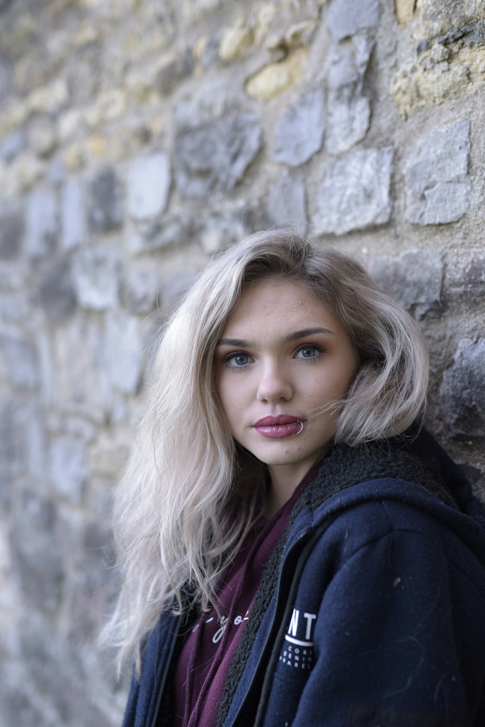 woman in black coat leaning on brown concrete wall