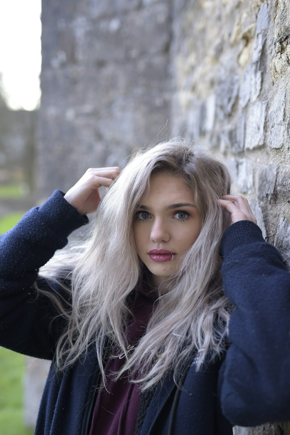 woman in blue long sleeve shirt leaning on brown concrete wall during daytime