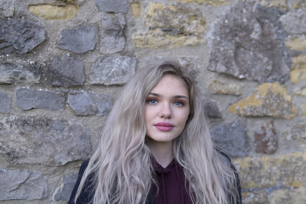 woman in black jacket standing beside gray wall