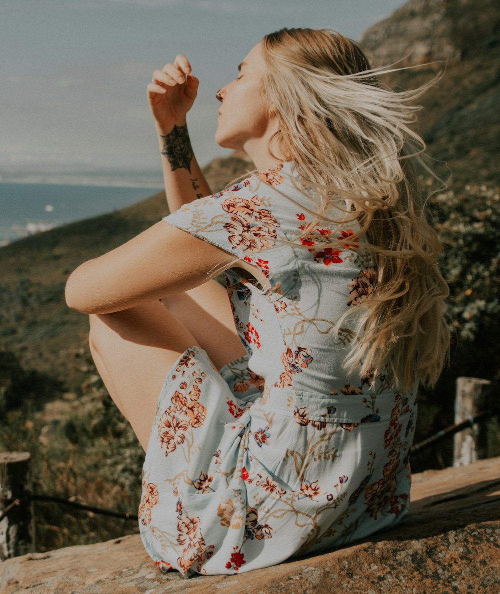 Mujer en vestido floral blanco, rojo y azul sentada en la cerca de madera marrón durante el día