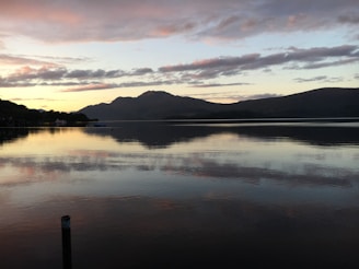 A tranquil lake reflecting the surrounding mountains at sunset.
