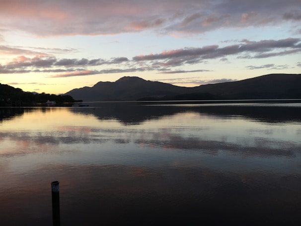 A tranquil lake reflecting the surrounding mountains at sunset.