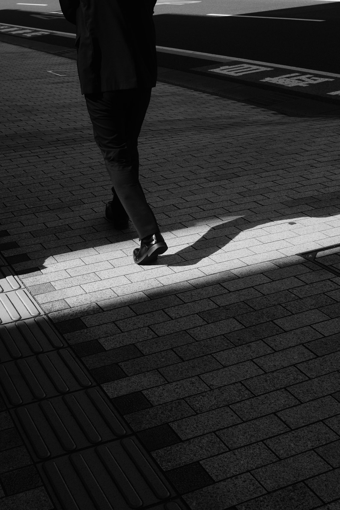 person in black pants and black shoes walking on sidewalk during daytime