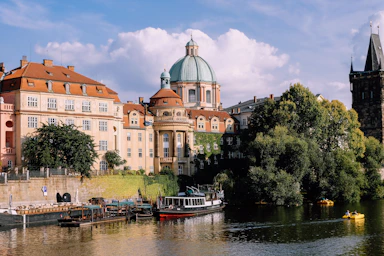 red and white boat on river near green trees and a brown concrete building in Prague during daytime