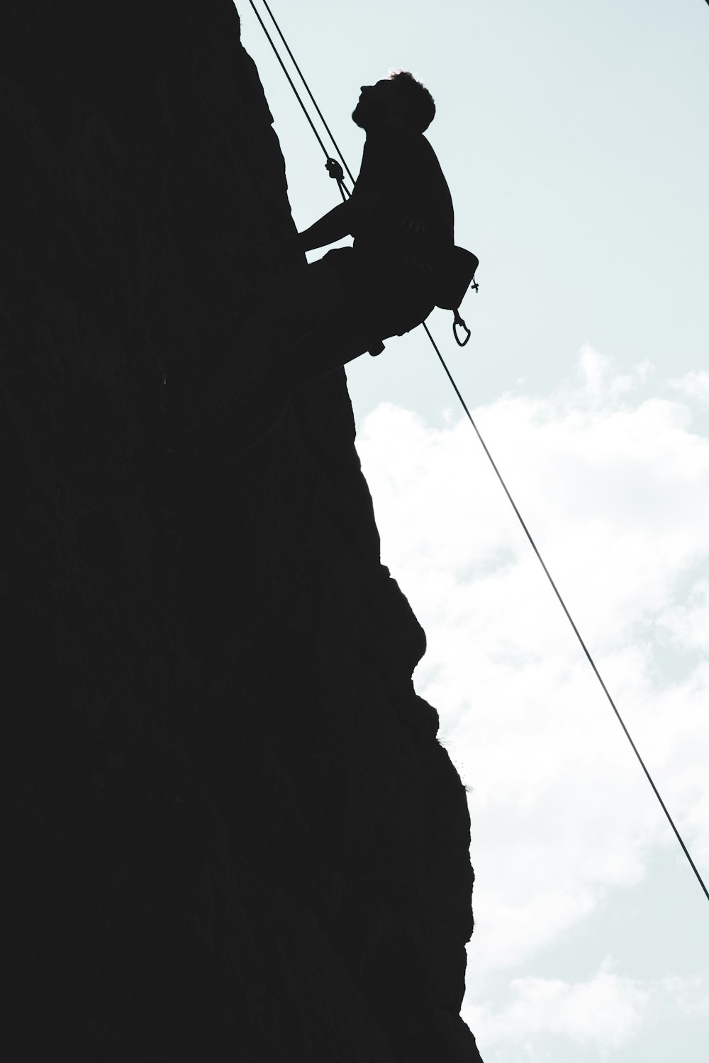 silhouette of man climbing on mountain during daytime