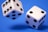 Two white dice with black dots displayed on a vibrant blue background. Both dice are in mid-air, showing the dynamic motion and interaction between the objects.
