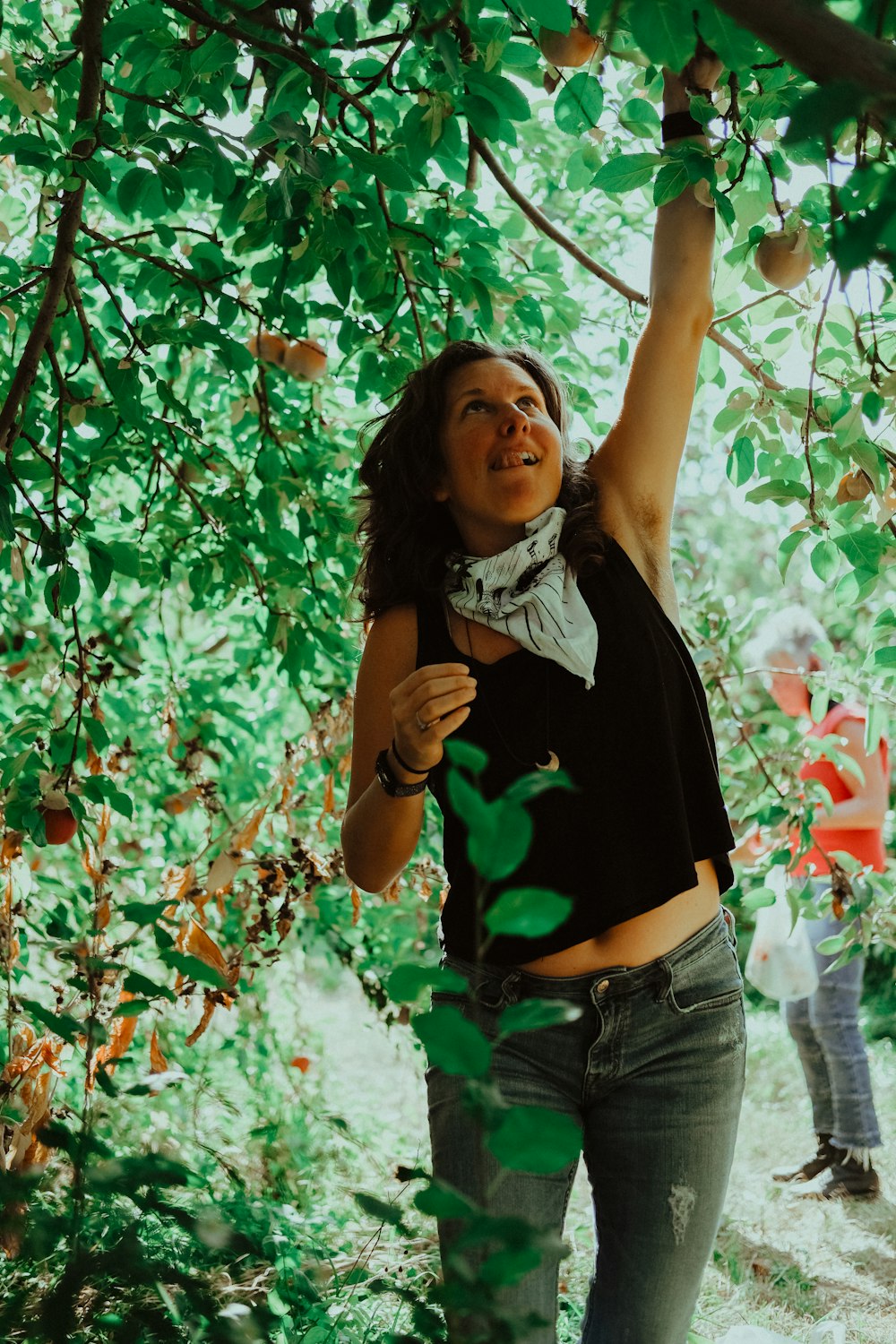 Mujer con camiseta verde sin mangas y pantalones cortos de mezclilla blanca de pie debajo de un árbol de hoja verde durante el día