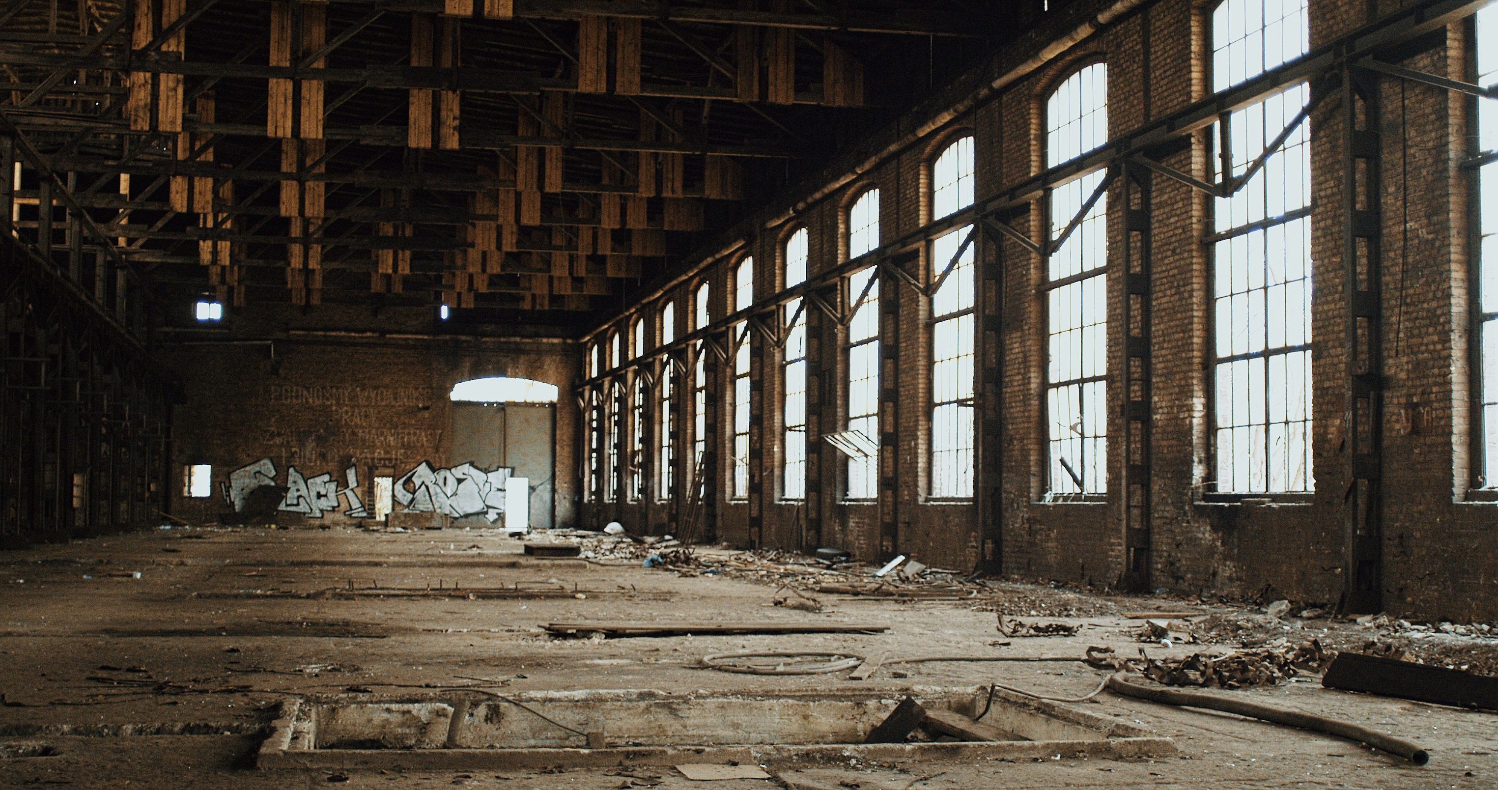 Large abandoned room with tall windows and debris on the ground