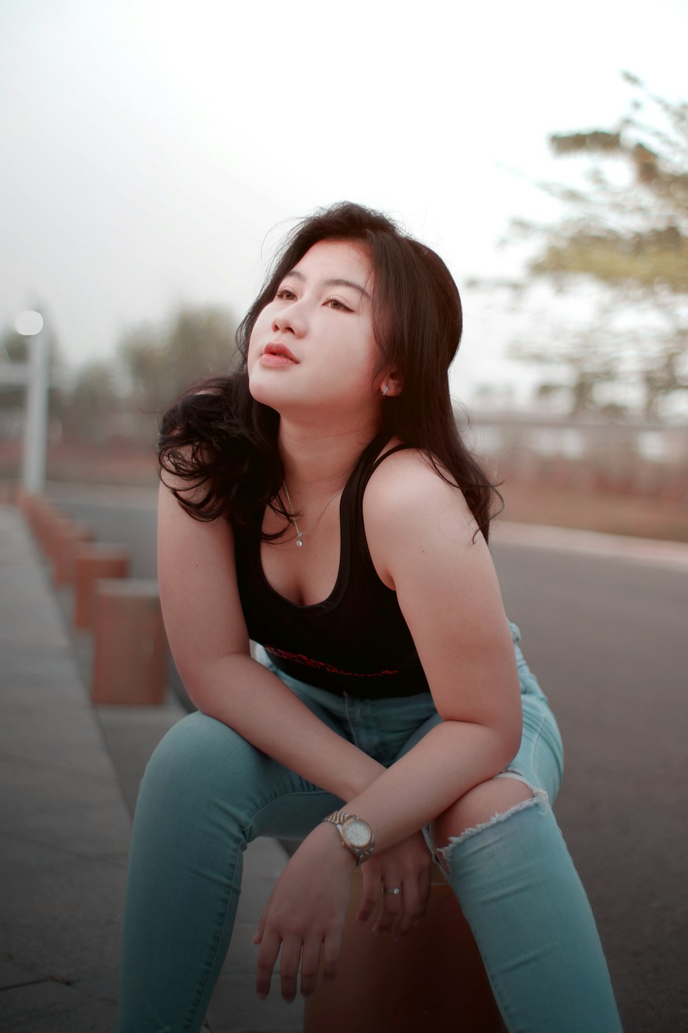 woman in black tank top and blue denim jeans sitting on gray concrete road during daytime