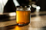 Close-up of a handcrafted glass jar filled with golden honey, resting on a rustic wooden table with soft natural light.