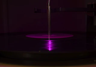 A moody studio shot with neon purple lighting highlighting mixing equipment and vinyl records.