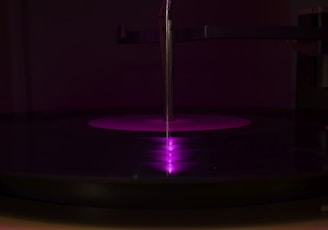 Close-up of a vinyl record spinning under dim purple lighting, casting deep shadows.