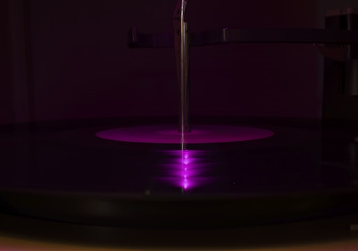 Close-up of a vinyl record spinning under dim purple lighting, casting deep shadows.