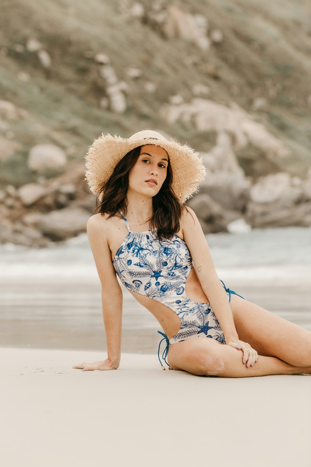 woman in blue and white floral bikini wearing brown sun hat sitting on beach shore during