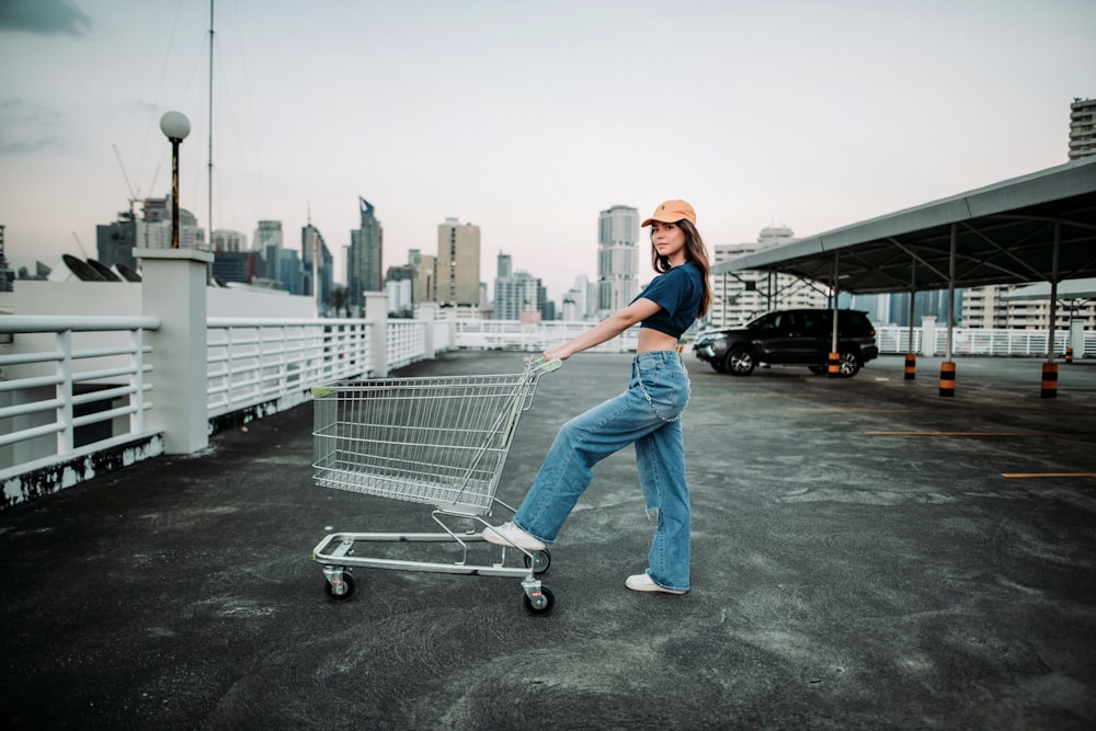 woman in blue denim jeans and white cap standing on gray shopping cart during daytime