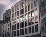 A multi-story building with large rectangular windows. The facade has a modern design with a sign displaying the word 'SPACES'. The sky is overcast, giving the scene a somewhat dim lighting.