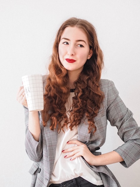 woman in gray cardigan holding white ceramic mug