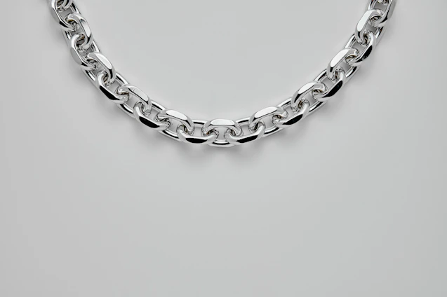 Close-up of a 92/8 silver-platinum chain glistening softly against a cream background, highlighting its intricate links and polished finish.
