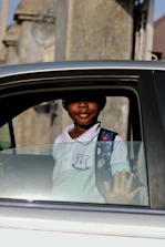 A friendly driver helping a child with a backpack into the car on a bright morning.
