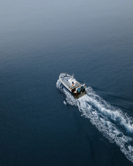 A sturdy fishing boat cutting through calm ocean waters under a clear blue sky.